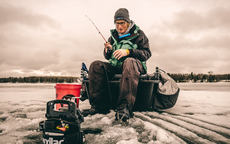 man ice fishing on frozen lake